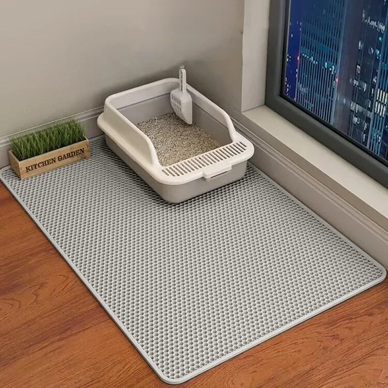 A large honeycomb cat litter mat is placed on a wooden floor near a window with a city view.