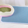 A pink and white double-layer cat litter mat with a green litter scoop resting on a blue textured mat.