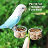 A white parrot is feeding from a transparent, clip-on food bowl mounted on a bracket.