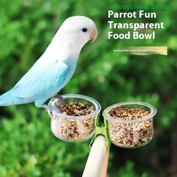 A white parrot is feeding from a transparent, clip-on food bowl mounted on a bracket.