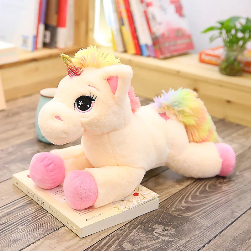 A fluffy white unicorn plush toy with pink accents and rainbow colored mane sitting on a wooden surface.