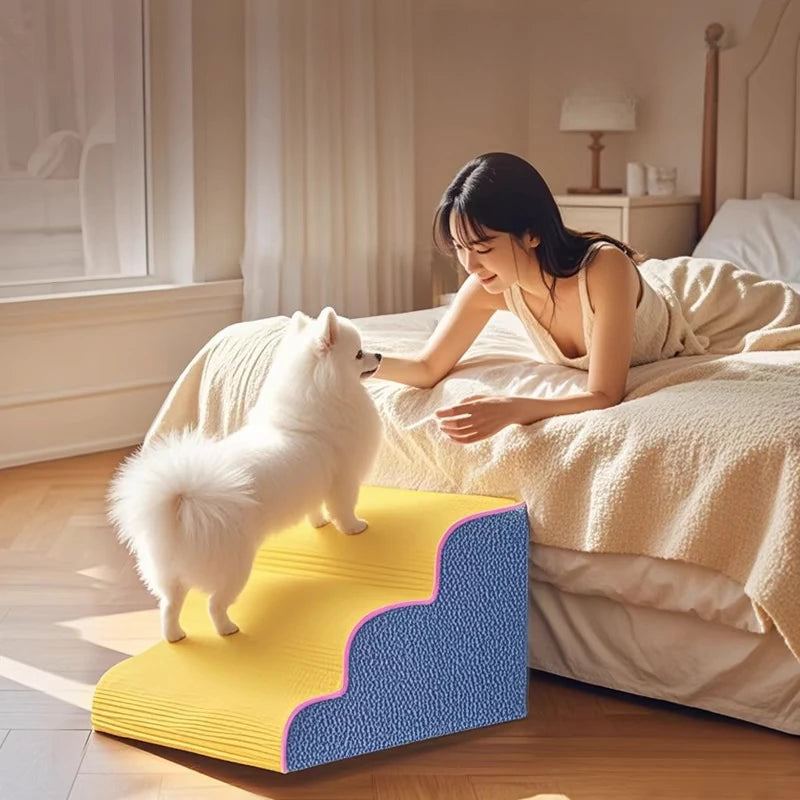 Un perro blanco está de pie en una rampa de juguete de espuma amarilla junto a una mujer relajándose en una cama.