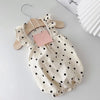 A cream-colored pet dress for a small dog featuring black polka dots, displayed on a wooden hanger.
