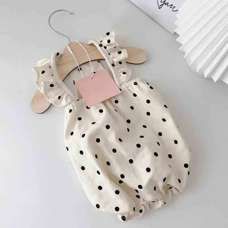 A cream-colored pet dress for a small dog featuring black polka dots, displayed on a wooden hanger.