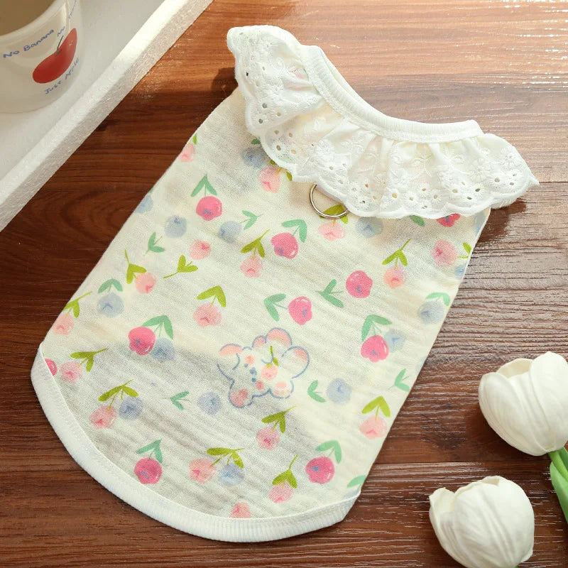 A light-colored cotton dog vest with a white lace collar and a pastel cartoon print lying on a wooden surface.