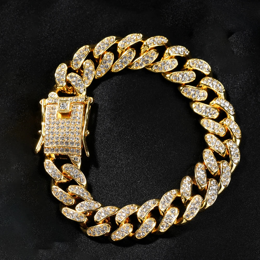 Pulsera de cadena cubana dorada con acento de straseo rectangular sobre fondo negro.