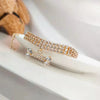 A close-up of a crystal rhinestone pet collar with a bone pendant resting on a white surface.