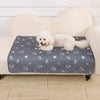 A fluffy white dog is lying on a gray pet pad placed on a light-colored sofa.