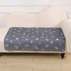 A gray pet pee pad with white paw prints is placed on a beige upholstered surface.