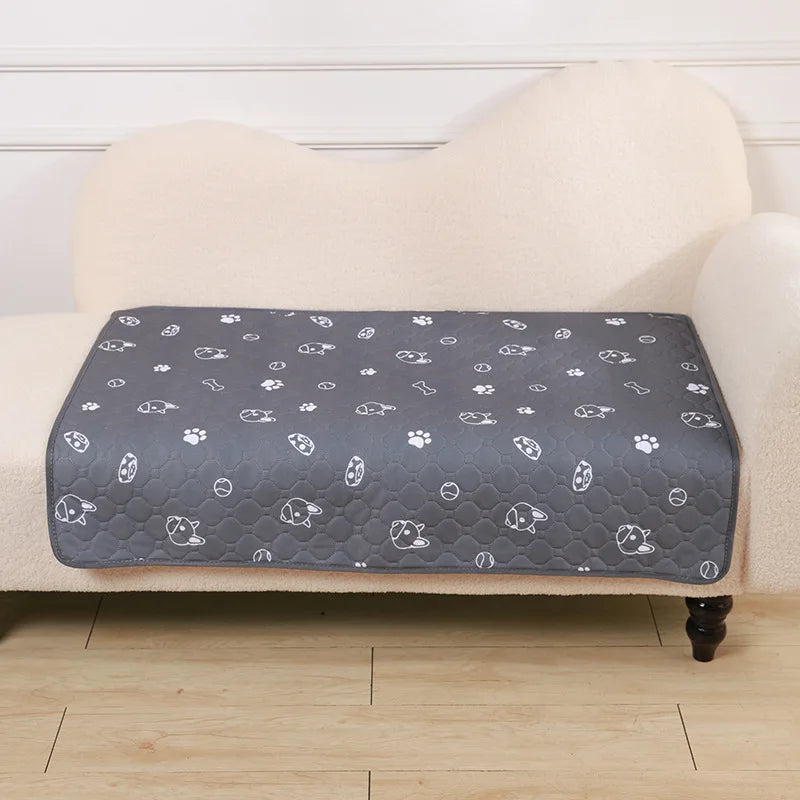 A gray pet pee pad with white paw prints is placed on a beige upholstered surface.