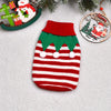 A knitted red and white striped dog sweater with green trim and white pom-poms, displayed near Christmas decorations.