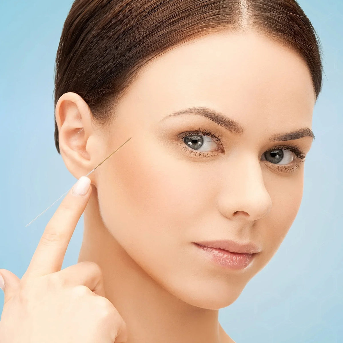A woman's hand is using a thin metal tool to clean or examine the ear, shown in a close-up portrait.