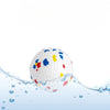 A white chew ball with colorful plastic inserts is submerged in clear water.