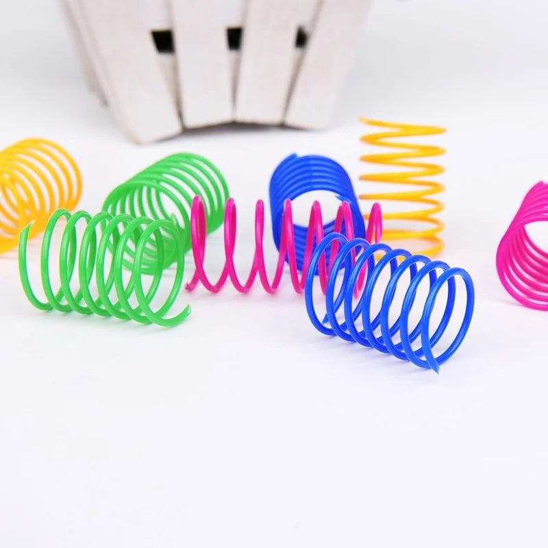Eine Sammlung farbenfroher, interaktiver Spiralkatzentoys in grün, pink, blau und gelb auf einer weißen Oberfläche.