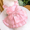 A pink satin pet dress with a bow and D-ring for a small dog is displayed on a white surface.