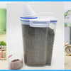 A clear airtight pet food storage container filled with dry kibble and a measuring cup nearby.