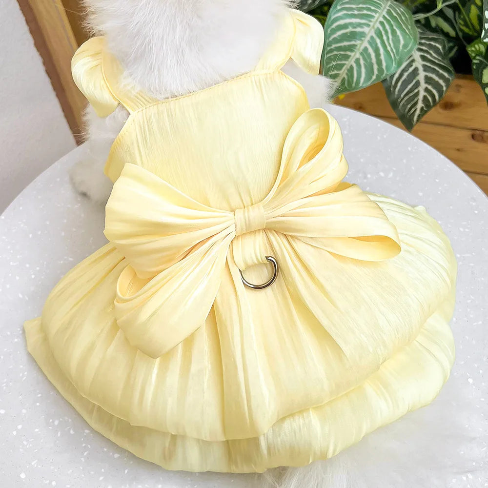 A yellow pet dress for a small dog featuring a bow detail and a D-ring.