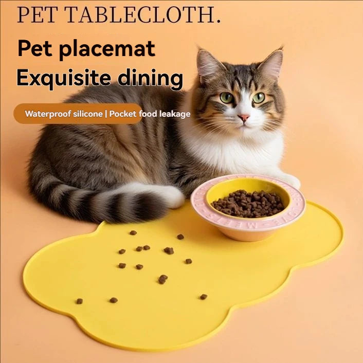 A fluffy tabby cat is sitting on a yellow silicone feeding mat with food pellets, demonstrating a pet tablecloth product.