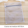 Bolsa de lavado blanca de malla cuadrada con cremallera gris sobre una superficie de madera.