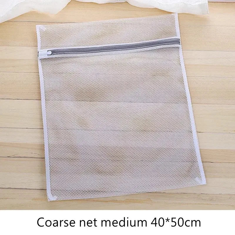 Bolsa de lavado blanca de malla cuadrada con cremallera gris sobre una superficie de madera.