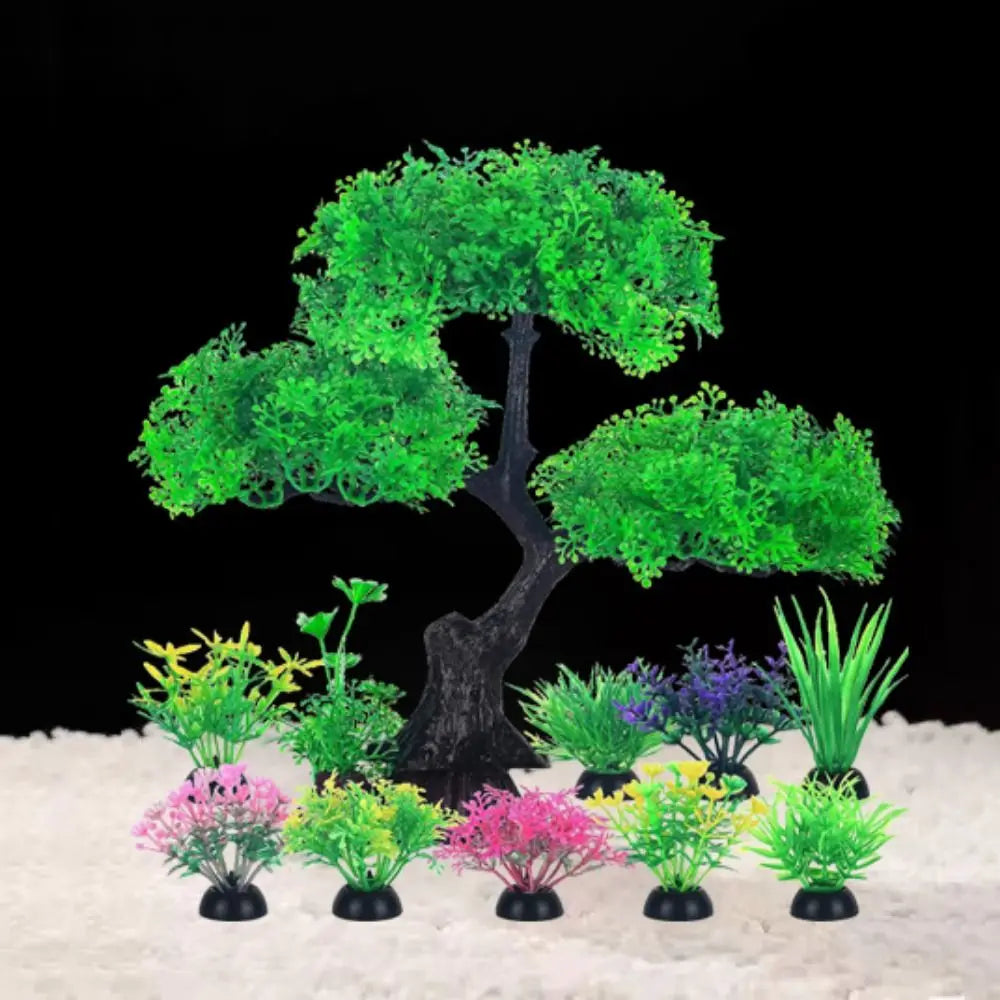 Un árbol artificial en miniatura con follaje verde vibrante y varias plantas en macetas pequeñas sobre una superficie blanca.