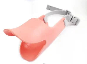 A pink adjustable silicone duckbill dog muzzle with a gray strap is shown against a white background.