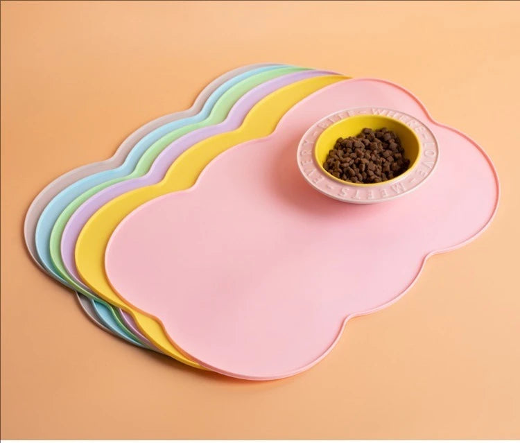 A stack of colorful silicone pet feeding mats, including a pink mat with a yellow mat underneath, holding a small bowl of pet