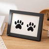 A black wooden photo frame displaying two black paw prints on a white background.