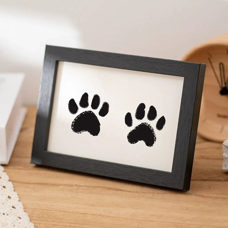 A black wooden photo frame displaying two black paw prints on a white background.