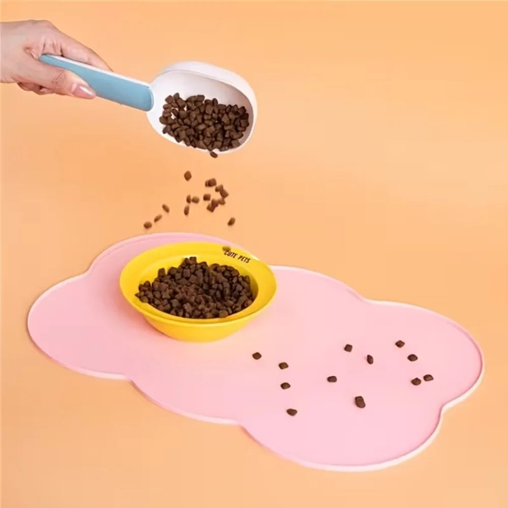 A hand is pouring dark pet food into a yellow bowl placed on a pink non-slip pet mat.