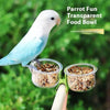 A white parrot is perched near a clear plastic food bowl attached to a clip-on feeder.