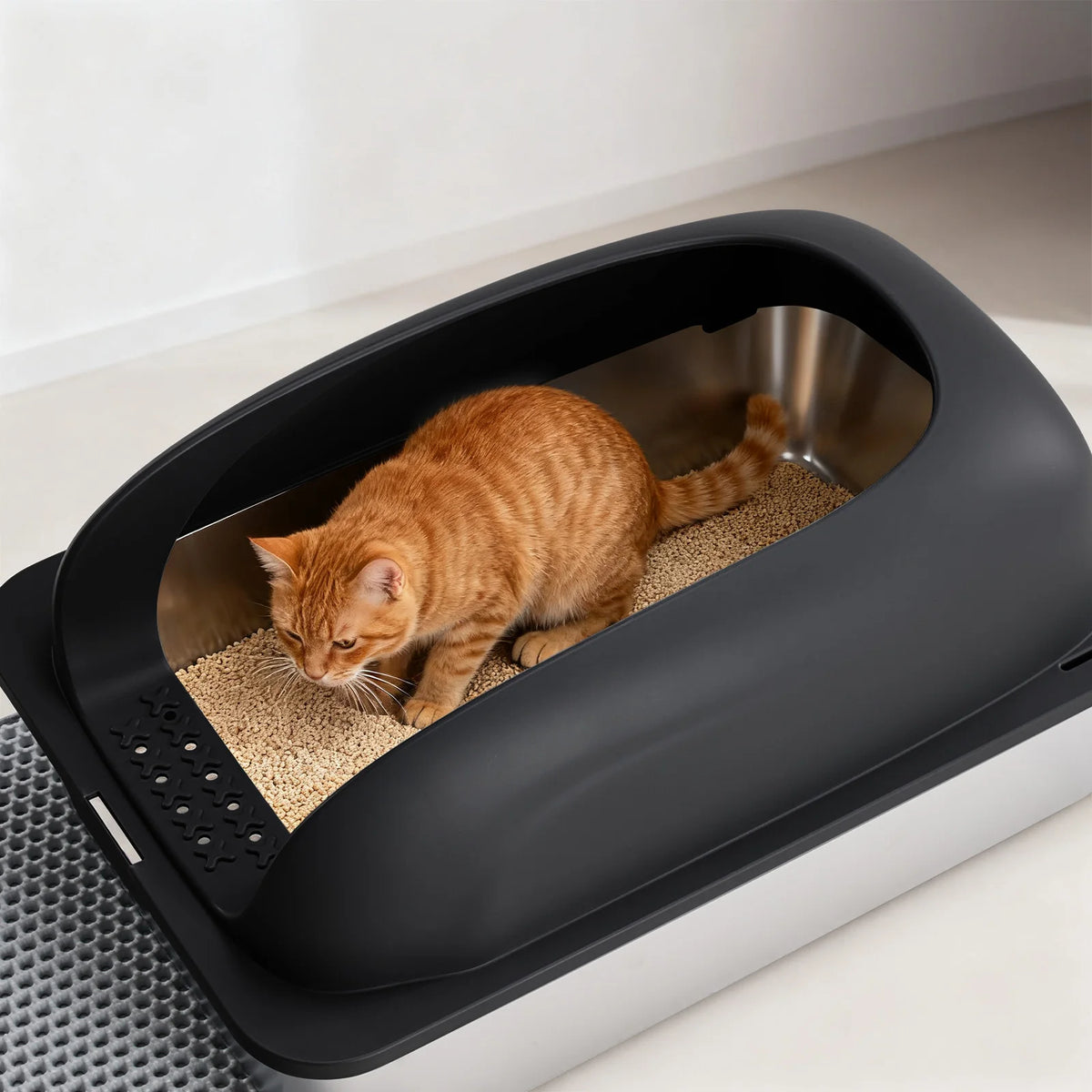 Une litière pour chat gris foncé avec un chat tigré orange, incluant un bol en acier inoxydable et un tapis.