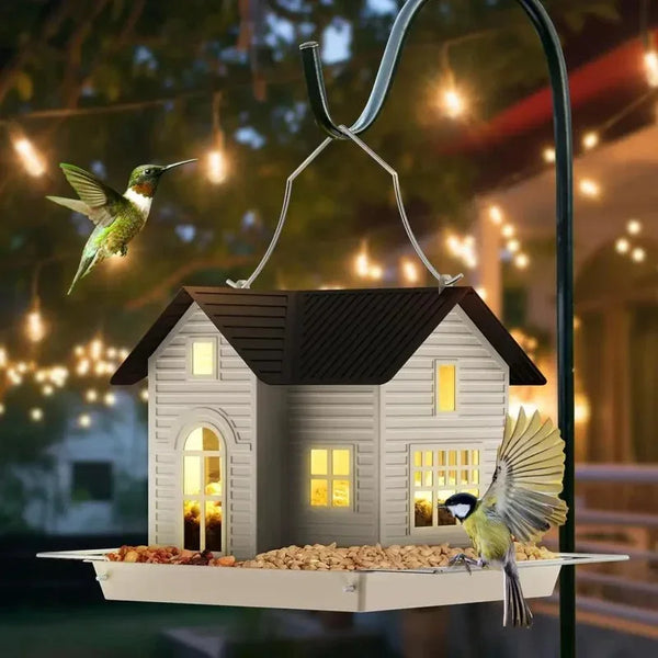 Solar-Vogelfutterlaterne mit Haus-Design, aufgehängt an einem Drahtseil an einem dunklen Pfosten.