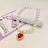 A pearl necklace with a gold pendant featuring a red heart, displayed on a purple card.