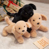 Three plush dogs, including a black puppy and two light tan puppies, are displayed on a white surface.