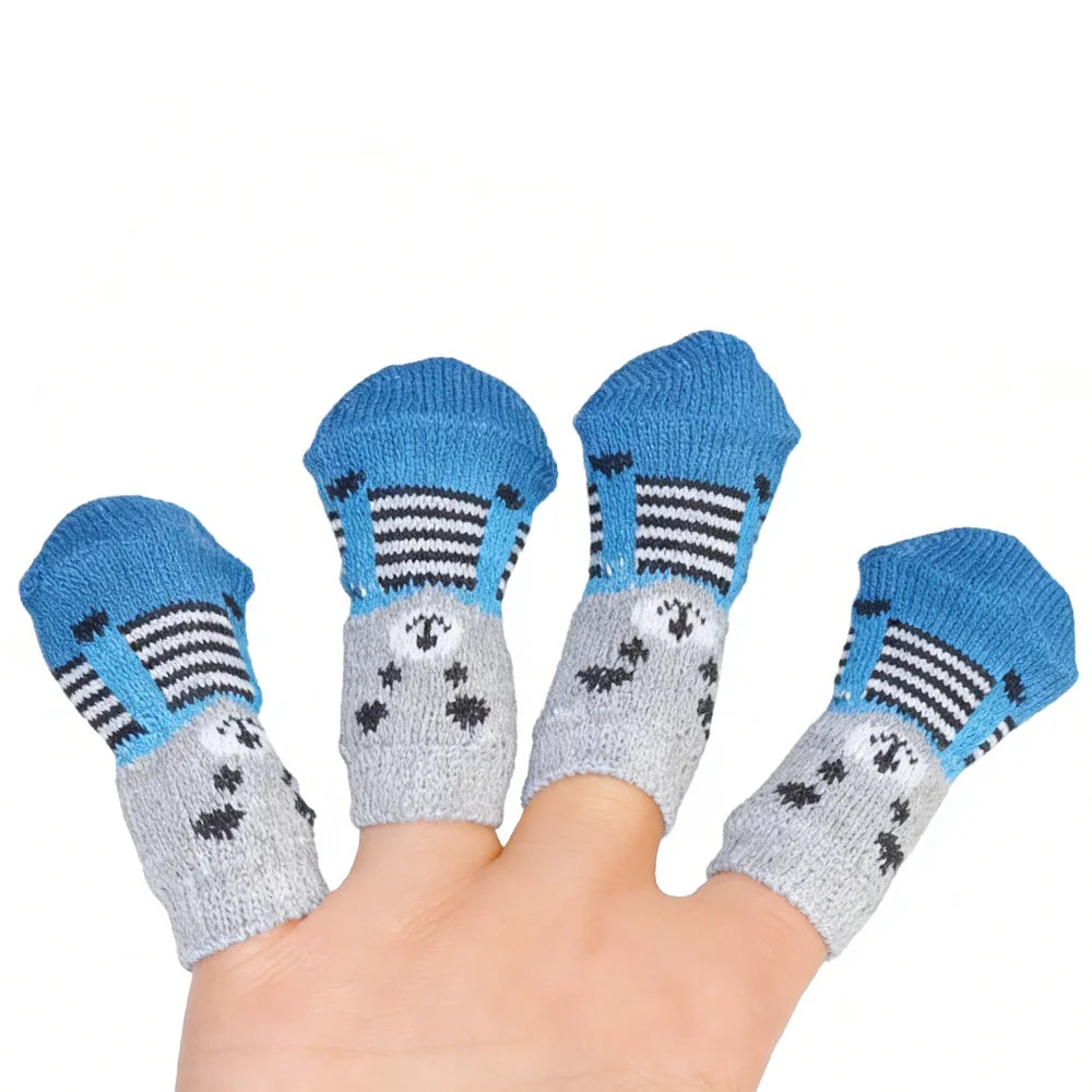 A hand is holding four pairs of anti-scratch cotton pet socks for small dogs and cats featuring blue, gray, and black stripes