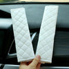 A pair of white quilted plush car seat belt shoulder protectors are held by a hand against a dark car interior background.