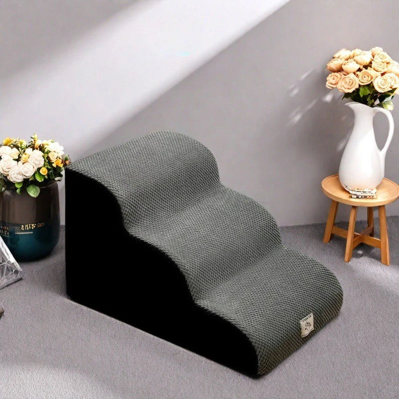 A dark gray washable non-slip pet stairs product placed on a light gray floor next to a vase of flowers.