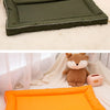 Two pet mats, one olive green and one orange, are shown next to a stuffed animal.