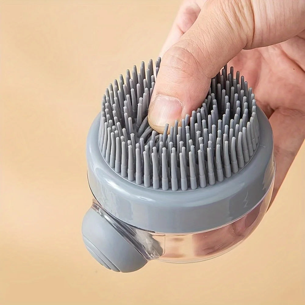 A hand is holding a grey pet bath brush with bristles and a dispenser for shampoo.