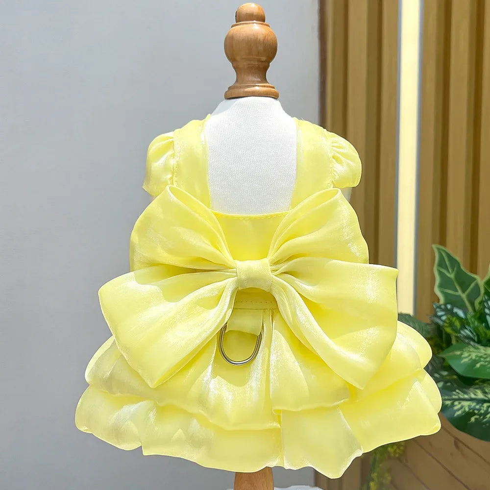 A yellow solid color pet dress with a large bow and D-ring for a small dog displayed on a mannequin.