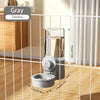 Un bol de mangeoire automatique pour animaux gris à gravité, à l'intérieur d'une cage en fil blanc, à côté d'un meuble en boi