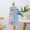 Light blue denim jacket with a crown embroidery and pink bow displayed on a wooden hanger.