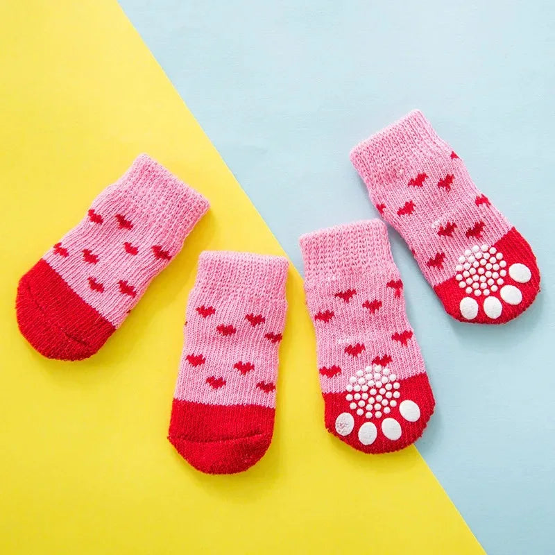 A set of pink and red knit dog socks with a tiger design laid on a yellow and blue background.