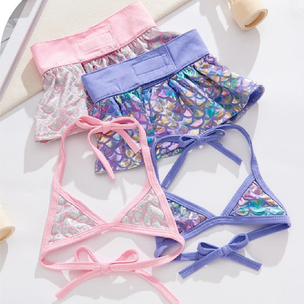 A collection of pink and purple summer pet swimsuits for dogs and cats laid out on a white surface.