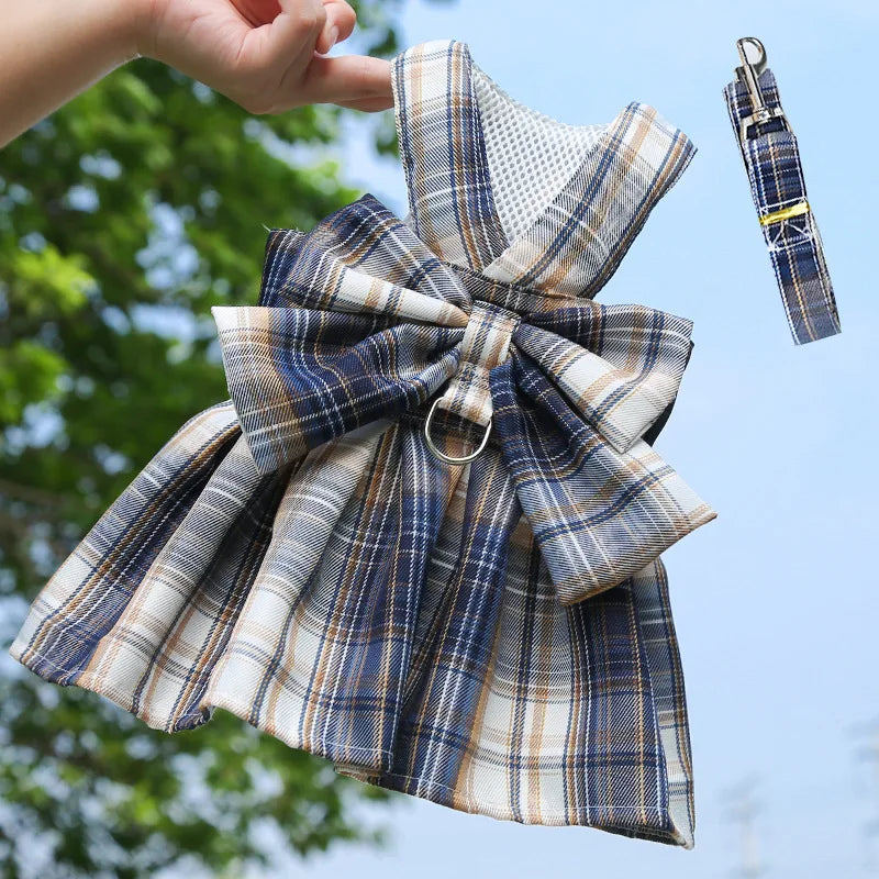 A plaid dog dress-up harness and clothes are being held by a hand against a bright blue sky.