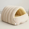 A beige plush cat cave bed with ribbed fabric and a removable inner lining is shown on a light surface.