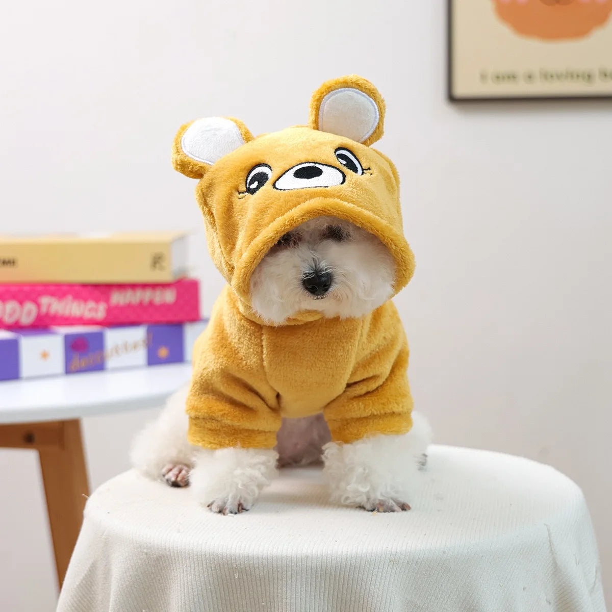 A fluffy, golden yellow seasonal flannel hoodie for a small dog sits on a white table.