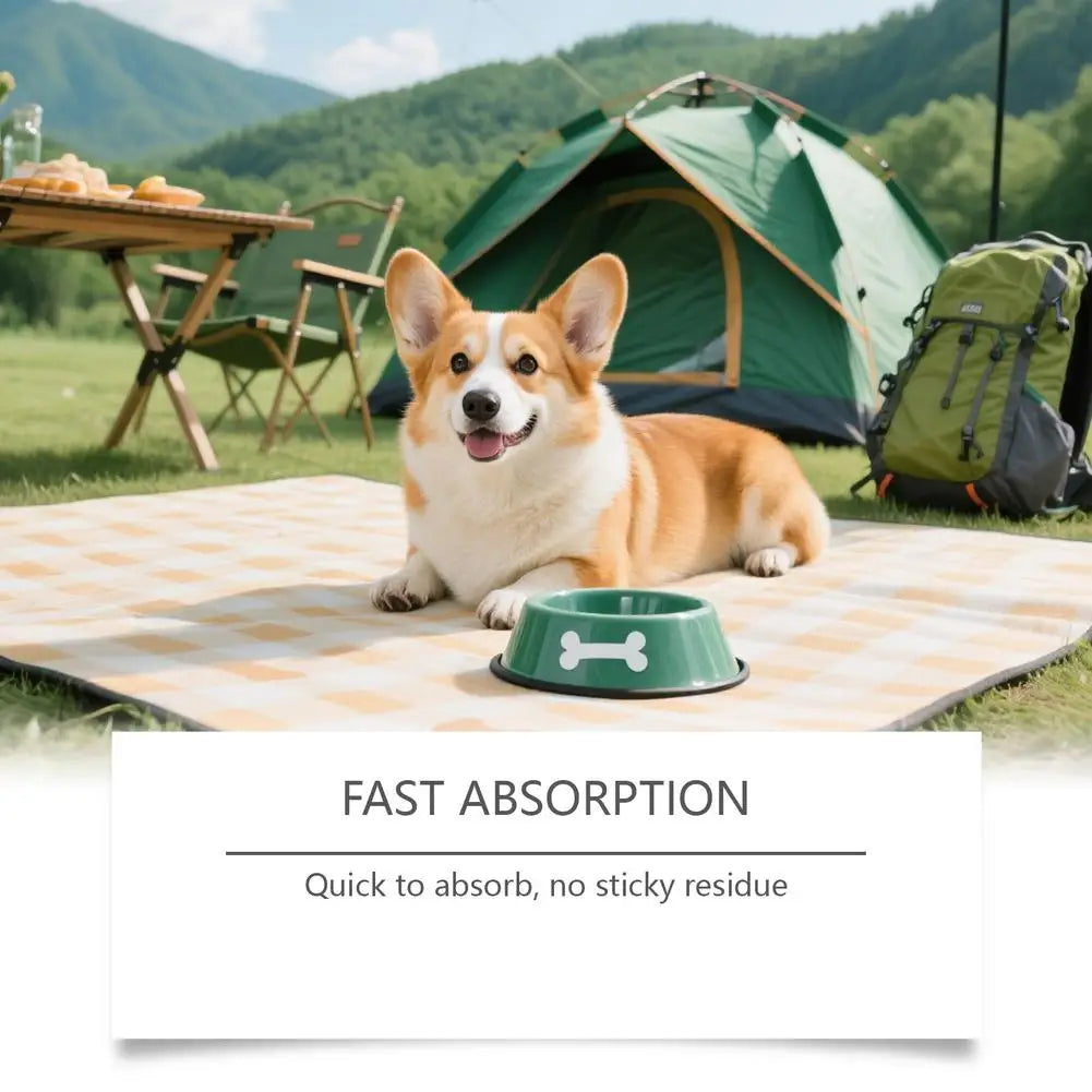 A happy dog lies on a checkered mat in a grassy field near a tent.