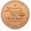 A round copper disk bird bath with a silhouette of a bird drinking water etched into it.